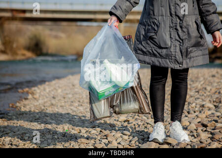 Müll in der Natur, in der die Reinigung der Umgebung im Frühjahr auf dem Fluss vom Müll eine Frau in Latex Handschuhe Blau in Blau, groß Stockfoto