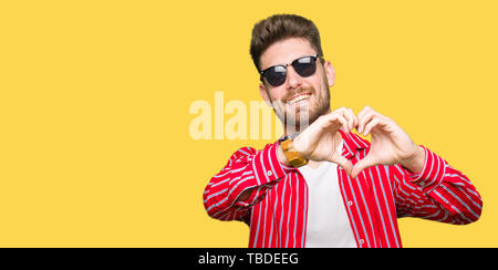 Junger stattlicher Mann mit Sonnenbrille in der Liebe mit Herz und mit Hand lächelnd. Romantische Konzept. Stockfoto