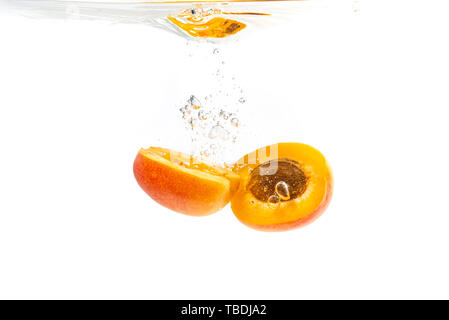 Frische reife Aprikose Split in der Hälfte in das klare Wasser fallen, auf weißem Hintergrund Stockfoto