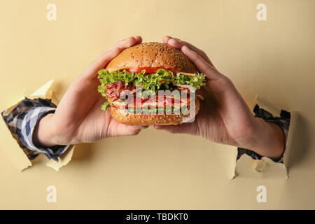 Weibliche Hände mit leckeren Burger auf farbigen Hintergrund Stockfoto