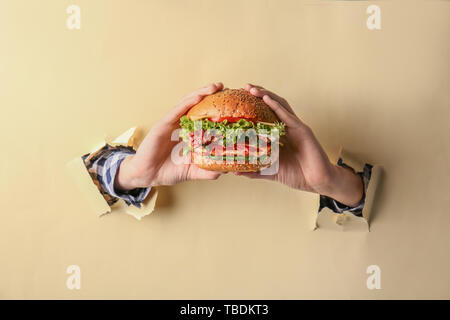 Weibliche Hände mit leckeren Burger auf farbigen Hintergrund Stockfoto