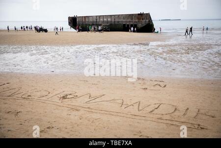 Frankreich. 01. Juni 2019, France (Frankreich), Arromanches-Les-Bains: Überreste des ehemaligen Hafen sind bei Gold Strand entfernt, hinter dem Schreiben "Normandie", die in den Sand geschrieben wurde. Nach der Landung der alliierten Truppen im Zweiten Weltkrieg, einer der zwei künstliche Häfen (Mulberry B) gebaut wurde an der Küste von Arromanches-les-Bains, durch die Truppen und liefert an Land gebracht wurden. 06.06.2019 ist der 75. Jahrestag der Landung der alliierten Truppen in der Normandie (D-Day). Foto: Kay Nietfeld/dpa Stockfoto