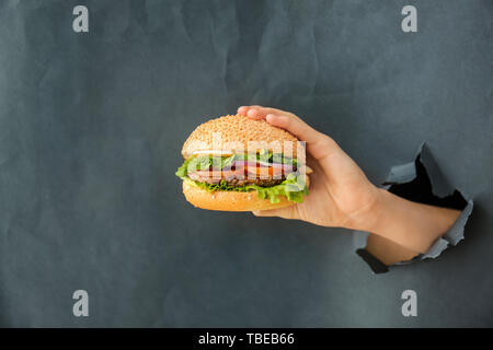 Weibliche hand mit leckeren frischen Burger auf grauem Hintergrund Stockfoto