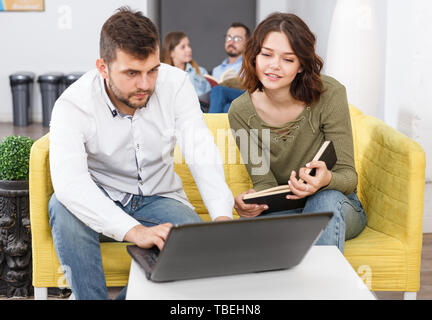 Paar junge Reisende mit Laptop Planung touristische Rundfahrt beim Stillstehen in Hostel Lobby Stockfoto