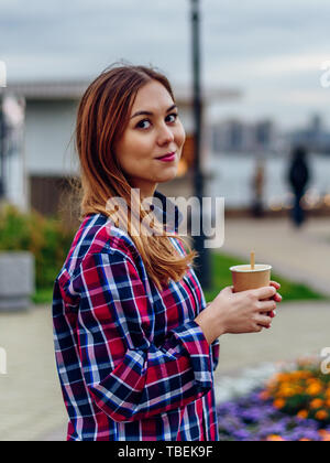 Kaffee unterwegs. Schöne junge Frau mit Tasse und lächelnd im Park Stockfoto