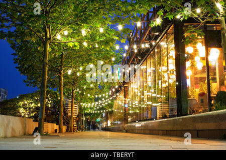 Dekoriert und beleuchteter Gehweg mit einer Reihe von Bäumen, an der blauen Stunde. Lichter aus sind die Bars und Restaurants in der Nähe von Fluss Dambovita, Bukarest, Stockfoto