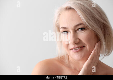 Reife Frau geben sich Massage auf hellen Hintergrund Gesicht Stockfoto