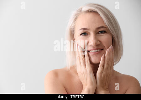 Reife Frau geben sich Massage auf hellen Hintergrund Gesicht Stockfoto