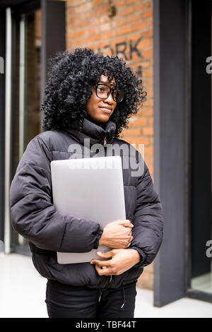 Junge Frau, die auf der Straße arbeiten, die auf Notebook- und Gespräch am Handy. Stockfoto