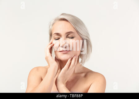Reife Frau geben sich Massage auf hellen Hintergrund Gesicht Stockfoto