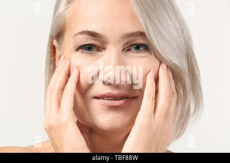 Reife Frau geben sich Massage auf hellen Hintergrund Gesicht Stockfoto