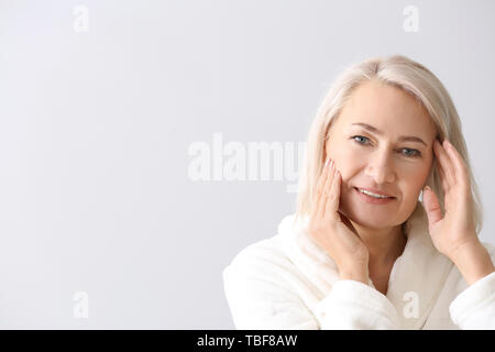 Reife Frau geben sich Massage auf hellen Hintergrund Gesicht Stockfoto