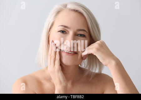 Reife Frau geben sich Massage auf hellen Hintergrund Gesicht Stockfoto