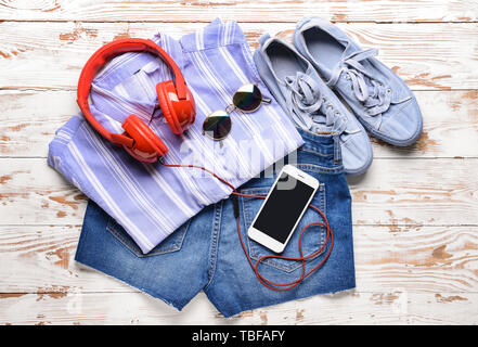 Weibliche Kleidung mit Kopfhörern und Mobiltelefon auf hölzernen Hintergrund Stockfoto