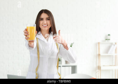 Portrait von weiblichen Ernährungsberaterin mit Glas Saft mit Daumen - oben in Ihrem Büro Stockfoto