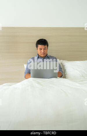 Junger Mann konzentrieren sich auf mit Laptop auf dem Bett Stockfoto