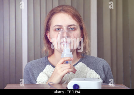 Junge Frau tut Inhalation Inhaliergerät für die Behandlung von Atemwegserkrankungen, nutzt sie Kompressor Vernebler System. Stockfoto