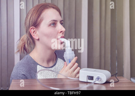 Junge Frau mit Asthma verwendet einen Zerstäuber, sie atmet durch das Mundstück, während die Maschine arbeitet. Der Nebel liefert ihr Asthma Medizin Stockfoto