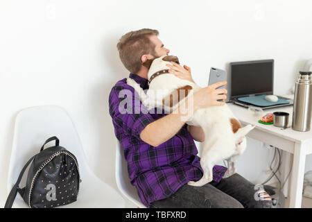 Menschen, Haustiere und Tiere Konzept - junge Mann umarmt Jack Russell Terrier und versuchen zu arbeiten Stockfoto