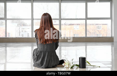 Frau mit leichenhalle urn und Lily Blumen im leeren Raum sitzen, Rückansicht Stockfoto