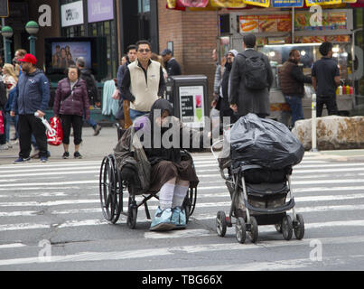 Eine wirklich haltbare ältere behinderte obdachlose Frau Kreuze 8. Avenue an der 42. Straße in einem Rollstuhl auch treibt einen Wagen voller ihre Sachen in New York City. Stockfoto