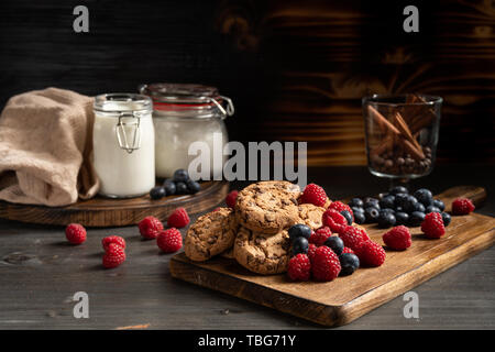 Cookies auf Holzbrett neben Beeren und Zimtstangen Stockfoto