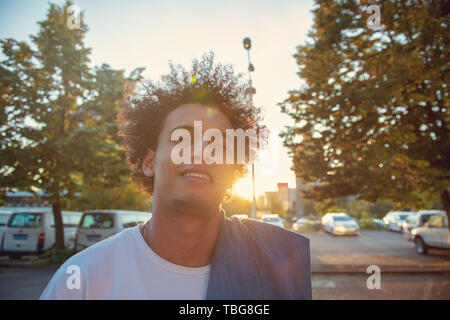 Glücklich lächelnde Urban Hipster junger Mann mit Smart Phone. Afrikanische amerikanische Teenager halten mobile Smartphone auf Sonnenuntergang mit Lens flare Stockfoto