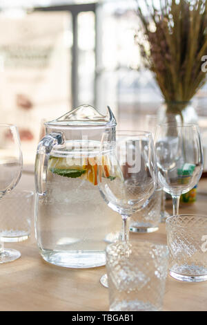 Krug mit hausgemachten Limonade Trinken von Mineralwasser, Zitrone, Orange und frische Minze auf Holztisch mit einer Menge Gläser Vordergrund, getrocknete Blumen Stockfoto