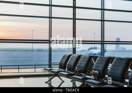 Blick auf Flughafen, interoir leeren Bank Stühle in der Abflughalle bei Sonnenaufgang. Flugzeug und Gebäude im Hintergrund. Reise und Verkehr Konzept Stockfoto