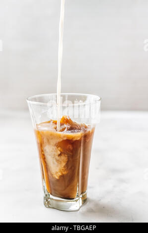 Eiskaffee mit Gießen Milch in Glas auf weißem Hintergrund Stockfoto