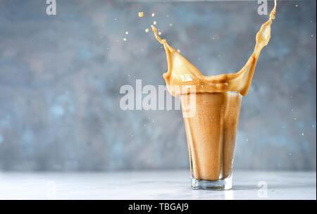 Big Splash in Glas Cappuccino auf blauem Hintergrund Stockfoto