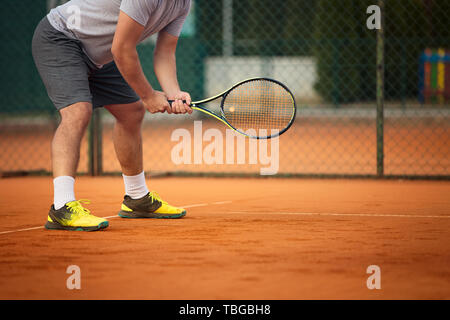 Der Mann hält Tennisschläger auf Sandplatz. Auf Gericht ist Sonnenuntergang. Mann mit Tennisschläger Stockfoto