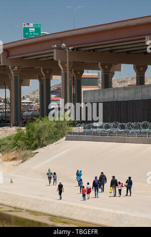 Eine Gruppe von Migranten, einschließlich Kinder, Spaziergang entlang der Ufer des Rio Grande in Richtung auf eine Lücke in der Wand unter einem neuen Autobahnbrücke in der Nähe von Dow Stockfoto