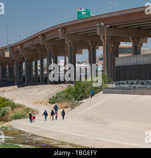Eine Gruppe von Migranten Spaziergang entlang der Ufer des Rio Grande in Richtung auf eine Lücke in der Wand unter einem neuen Autobahnbrücke in der Nähe von Downtown El Paso, Texas, Stockfoto