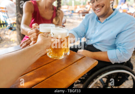 Freunde im Biergarten trinken, ein Mann im Rollstuhl Stockfoto
