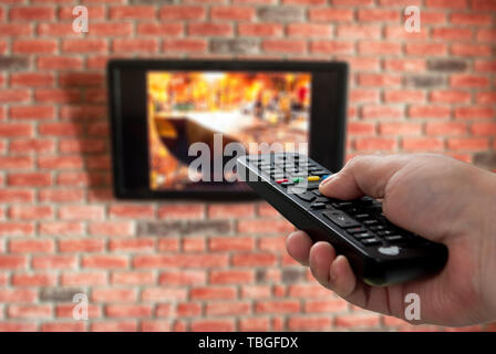 TV-Fernbedienung in der Hand und die Mauer im Hintergrund, die für den Hintergrund Stockfoto