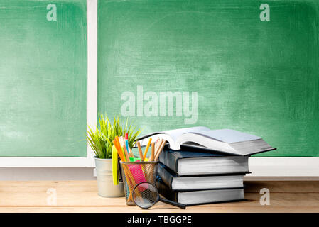 Stapel Bücher mit Topfpflanzen und Bleistifte in Korb Container mit Lupe auf dem Holztisch mit schiefertafel Hintergrund. Zurück zu Schule c Stockfoto