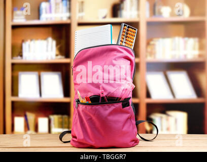 Rosa Rucksack mit Buch- und anderen Schreibwaren auf dem hölzernen Tisch in der Bibliothek. Zurück zu Schule Konzept Stockfoto