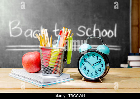 Stapel von Notebooks mit Apple und Bleistifte in Korb Container mit grünen Hefter und Wecker auf dem hölzernen Tisch mit blackboard Hintergrund. Back t Stockfoto