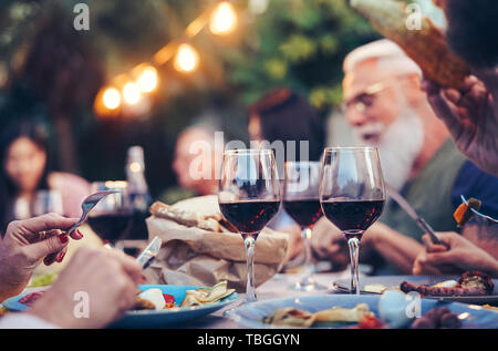 Happy Family Essen und Trinken roten Wein zum Abendessen Grillen im Freien - ältere und junge Menschen zusammen Speisen auf der Dachterrasse Stockfoto