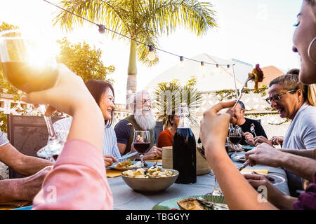 Glückliche Familie, ein Abendessen bei Sonnenuntergang Zeit im Freien - Gruppe von diversen Freunden Spaß speisen zusammen außerhalb Stockfoto
