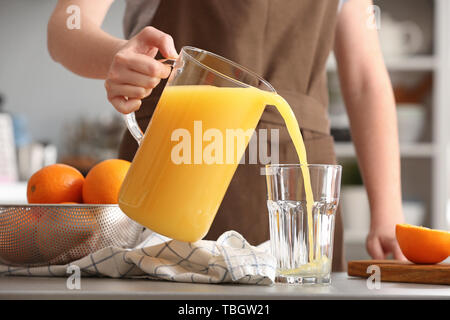 Frau gießen Orangensaft aus Kanne in Glas in der Küche Stockfoto