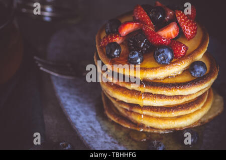 Pfannkuchen mit frischen Beeren und Ahornsirup auf dunklem Hintergrund. Klassische amerikanische hausgemachtes Frühstück. Stockfoto