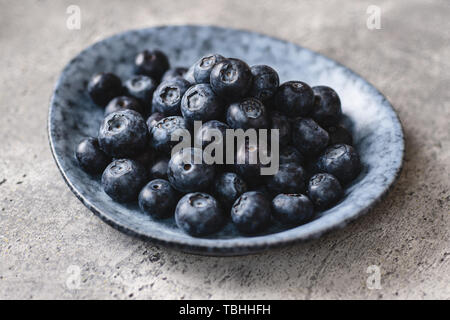 Frische organische Blaubeeren in graue Platte auf dunklem Stein Hintergrund Stockfoto