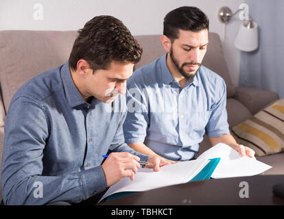 Zwei ernste Männer Arbeiten mit Dokumenten, während auf dem Sofa zu Hause sitzen Stockfoto