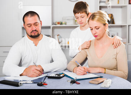 Zeitform Eltern schreiben von Dokumenten zu Hause Tabelle mit traurigen Sohn hinter Stockfoto