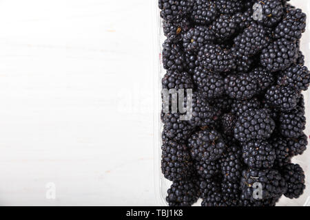 Brombeeren in einem Kunststoffbehälter auf weißem Holz- Hintergrund. Platz für Text Stockfoto