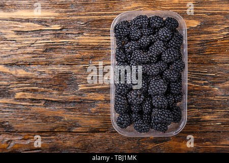 Brombeeren in einem Kunststoffbehälter auf braunem Holz- Hintergrund. Platz für Text Stockfoto