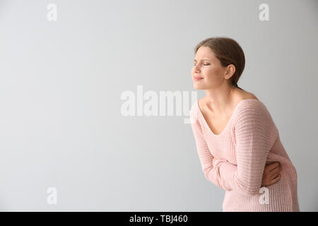 Junge Frau leidet unter Schmerzen auf hellen Hintergrund Stockfoto