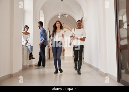 Zwei Positivität stilvolle weibliche Studenten nach Hause von Vortrag auf dem langen Flur. Gerne Afrikanische und kaukasische Freunde zusammen studieren an der internationalen Schule. Mitschüler für den Hintergrund. Stockfoto